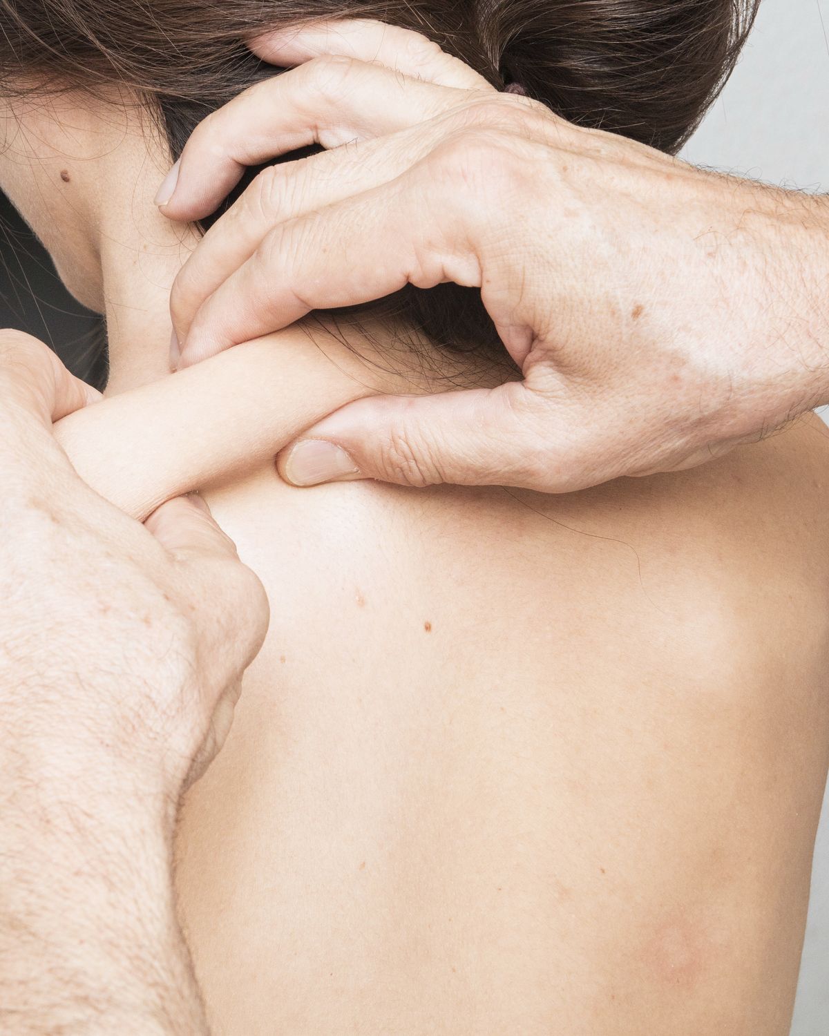 A clinician’s hands assessing a patient’s neck and shoulder